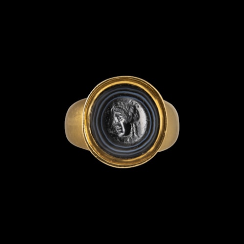A Roman banded agate intaglio set in a gold ring. Mask.